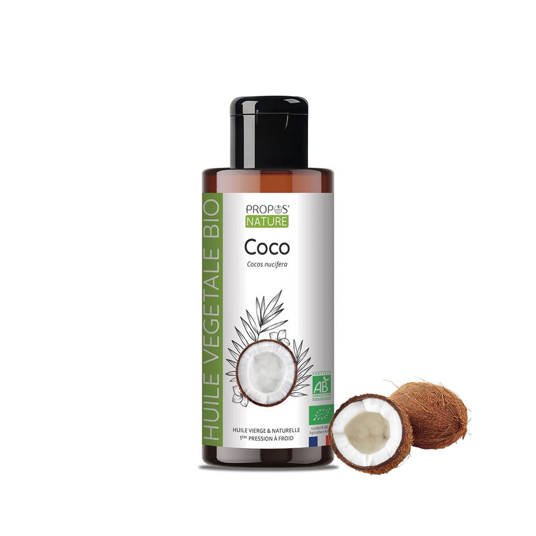 A bottle of Propos Nature Bio Organic Coconut Oil next to two coconuts on a plain white background.