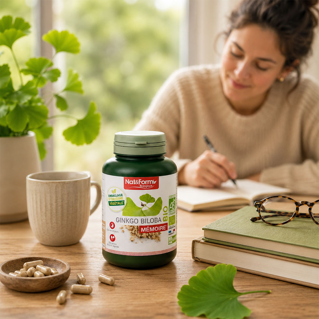 Bottle of Nat&Form Ginkgo Biloba supplement on a table with a woman writing in the background