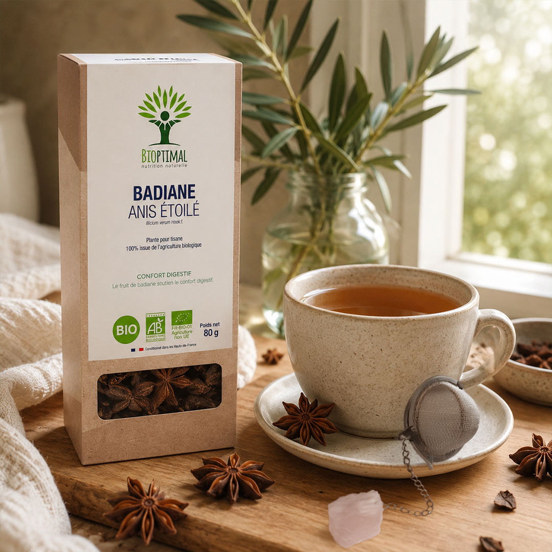 A box of BioPimal Badiane Anis Etoile herbal tea stands on a wooden table beside a cup of tea on a saucer, with star anise scattered around and a window in the background.