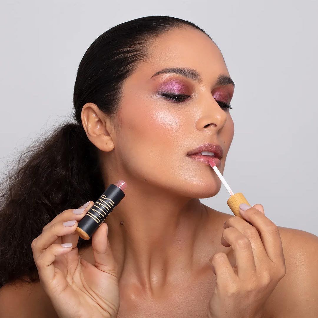 Woman applying Baims lipgloss against a plain background - Elliotti