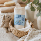 A set of soft baby washcloths in a woven basket, styled with a plush bunny toy, a wooden brush, and eucalyptus branches in a warm, neutral-toned setting. The brand 'Zélio' is visible on the label.