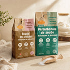 Two bags of Sodim Percarbonate and Soda Crystals are displayed on a light wooden surface with a wooden scoop of white soda crystals in front. The left bag is brown with a pink label, and the right bag is teal with a green label.
