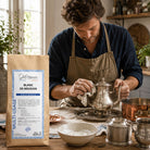 Man cleaning silverware with a bag of Blanc de Meudon powder on a wooden table.