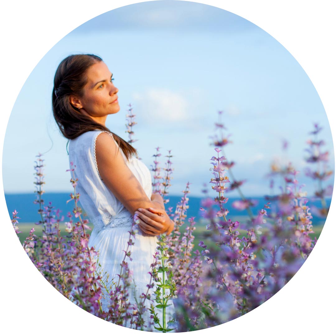 A woman standing in a field of clary sage flowers looking dreamy