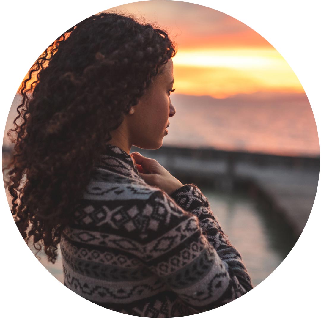 A woman standing by the water looking out to the sea in sun set