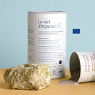 Epsom salt canister with a rock and spilled powder on a beige surface with a light blue background