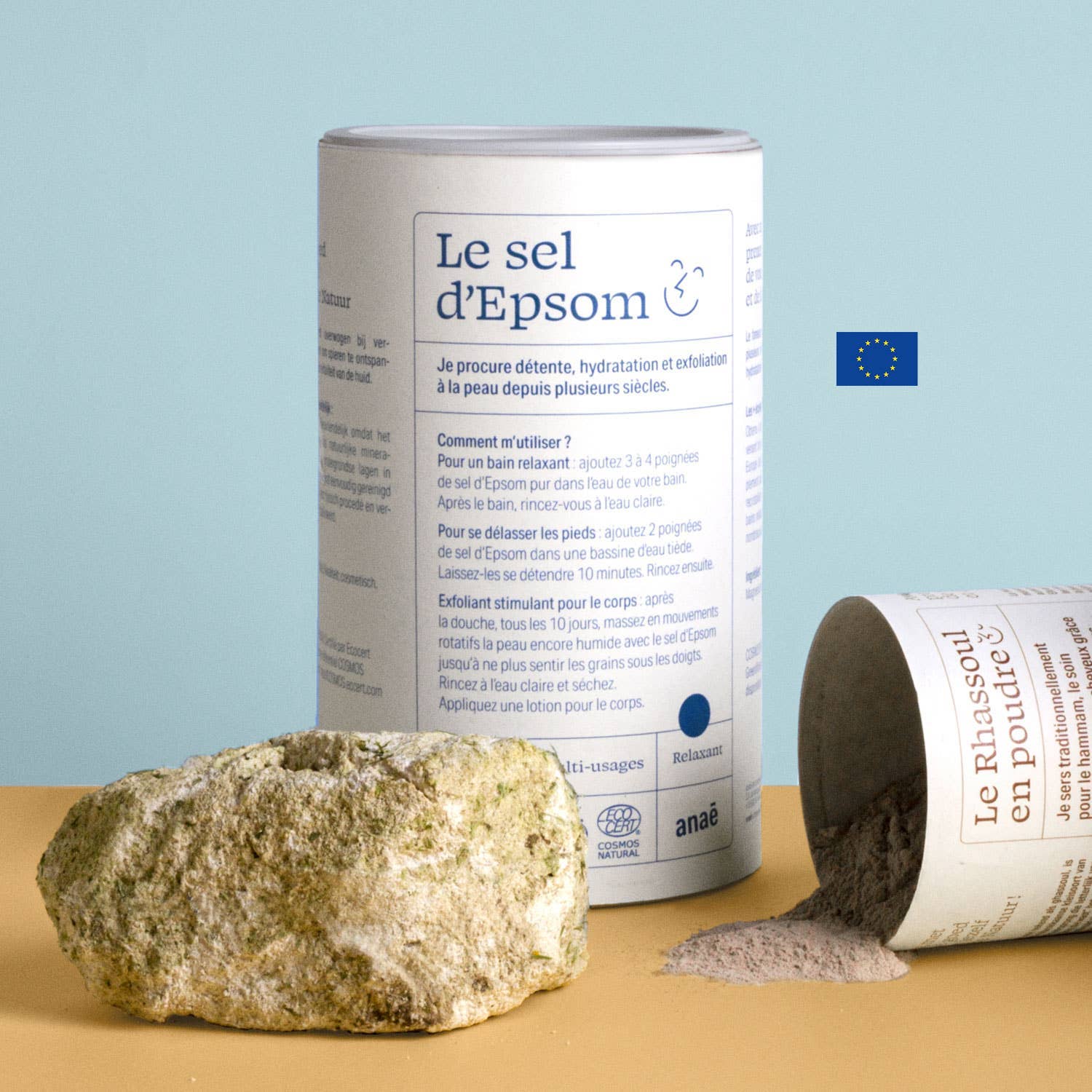 Epsom salt canister with a rock and spilled powder on a beige surface with a light blue background