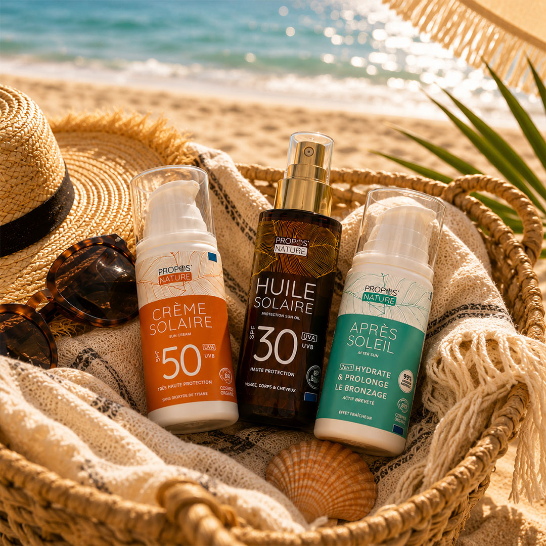 Sunscreen products and beach accessories in a woven basket on a sandy beach.