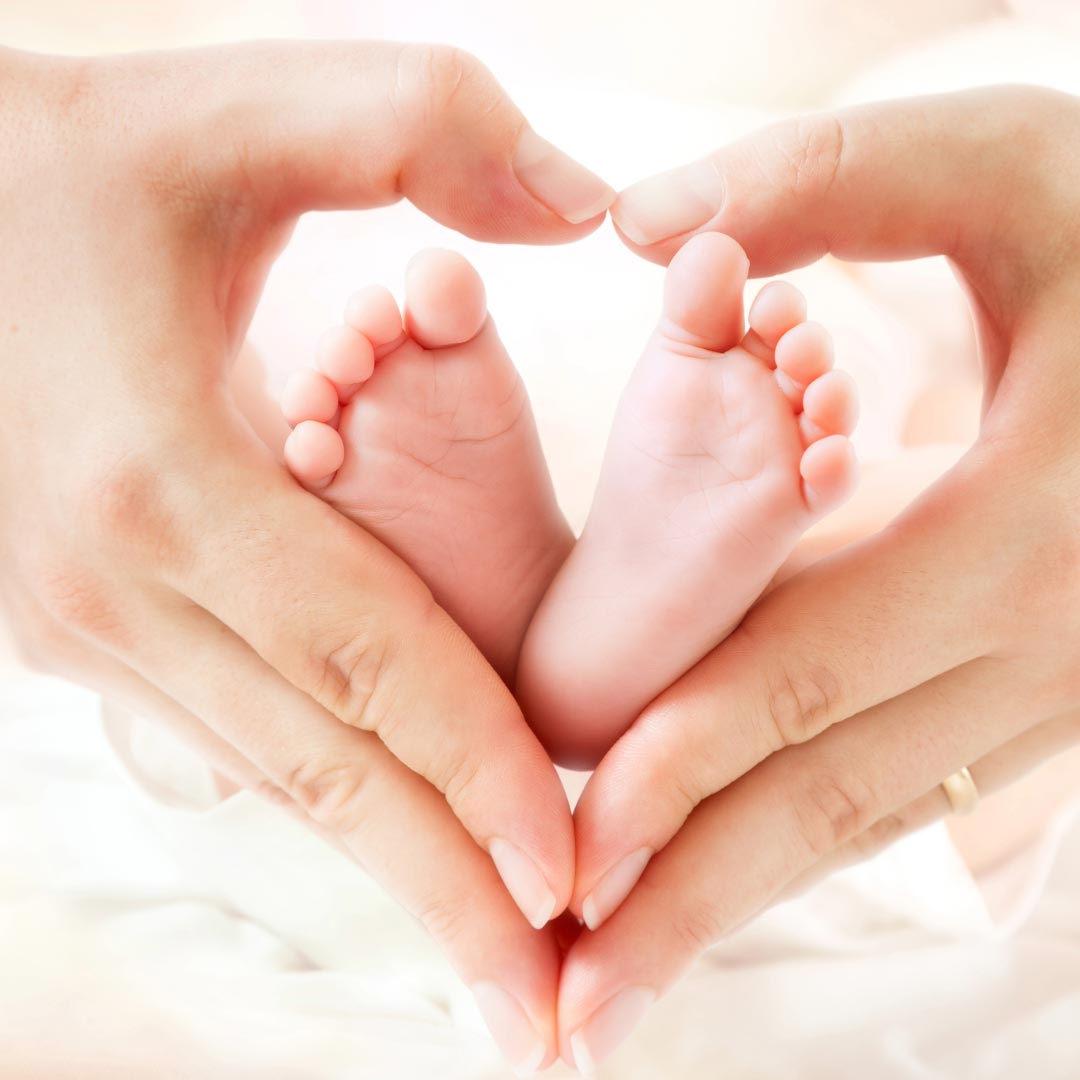A womans hands shaping a heart with small baby feet in the middle
