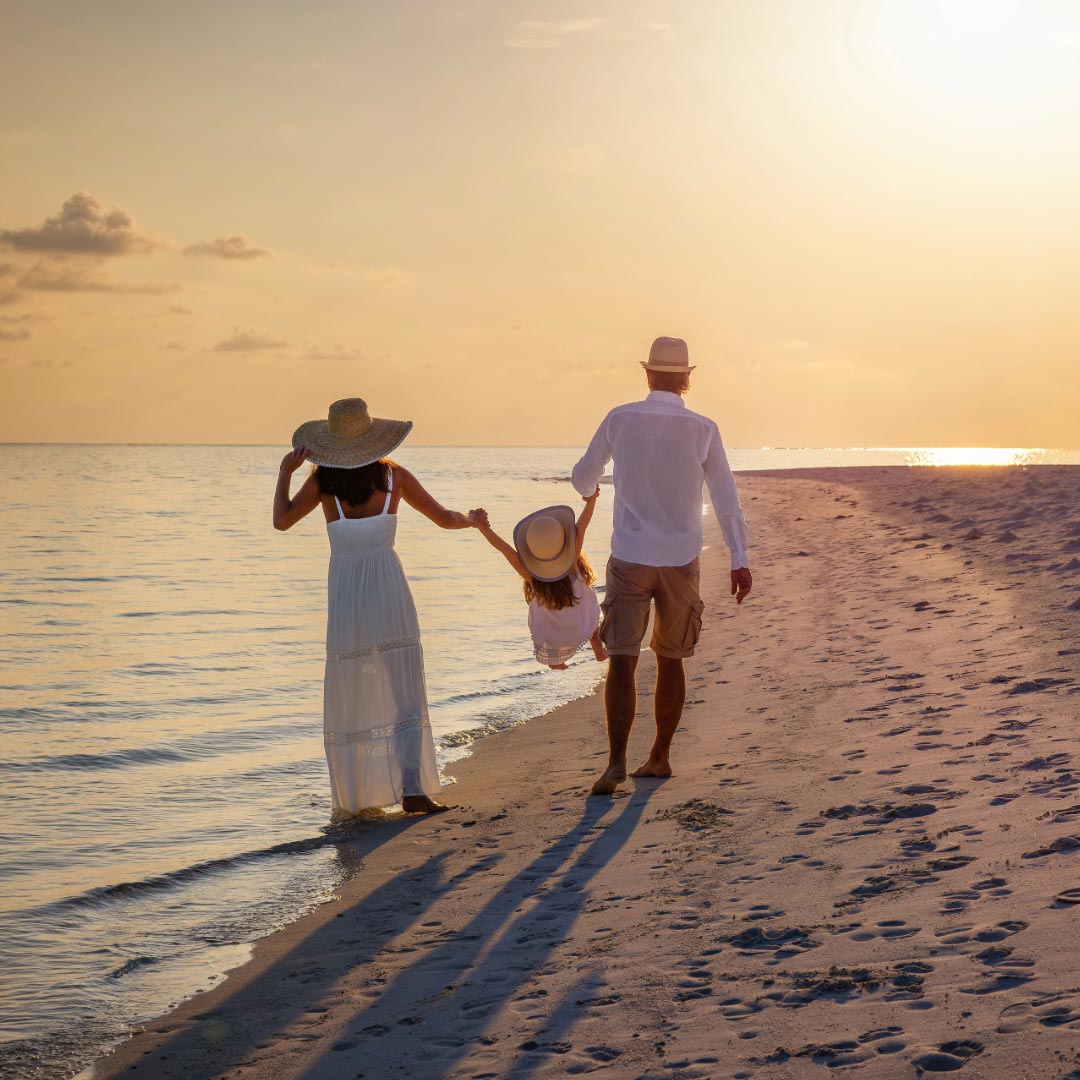 A couple walking on the beach at sunset holding a child between them