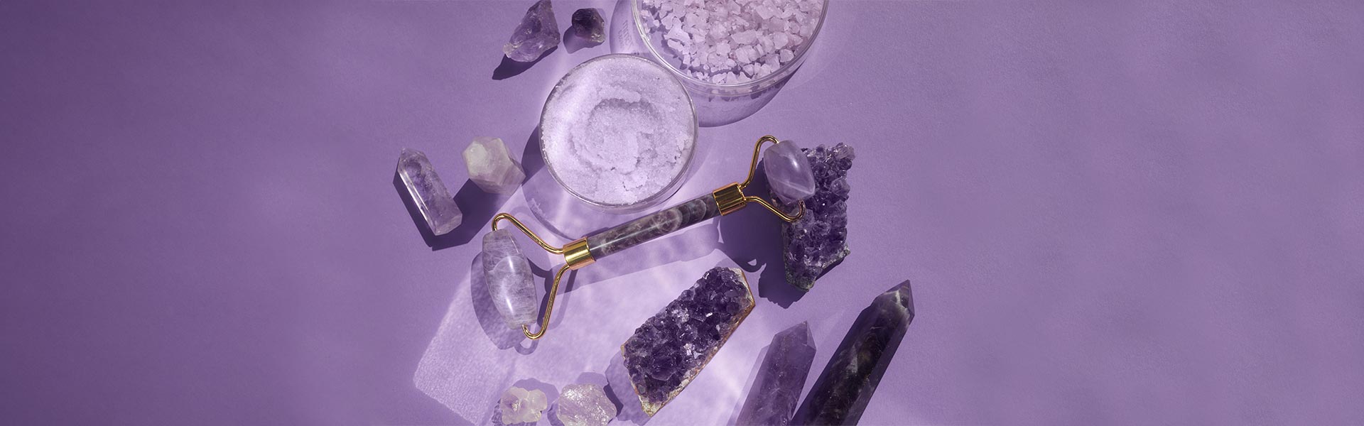 A Chi face roller Amethyst laying on a table on some Amethyst clusters, and other amathyst stones