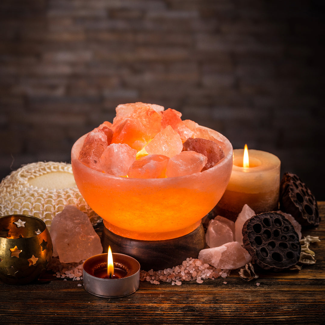 Himalayan salt lamp with candles and crystals on a wooden surface