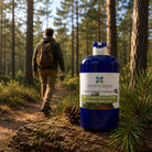 A blue bottle of essenciagua Pin Sylvestre de Lozère hydrosol stands on a mossy log in a forest, with a man hiking in the blurred background.